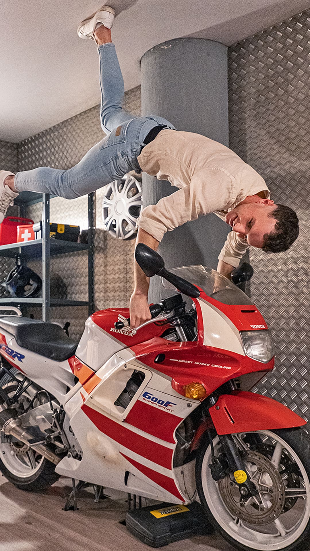 Un jeune homme en équilibre à l'envers sur une moto de sport Honda rouge et blanche fixée au plafond d'un garage à Upside Down House Barcelona